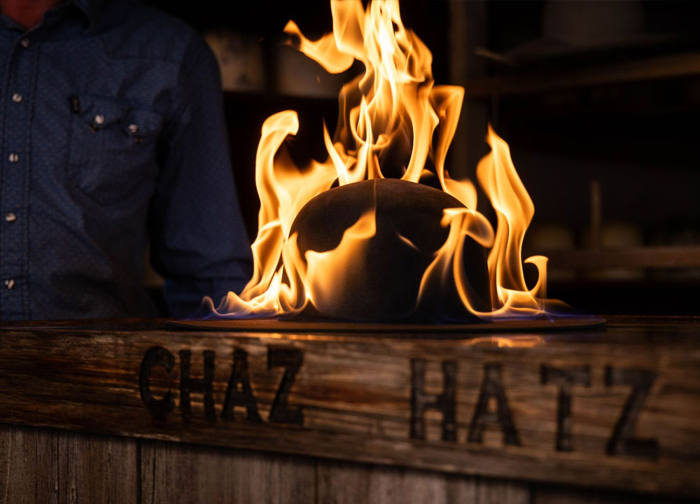 A wood sign reading Chaz Hatz with a cowboy hat on fire on top of the sign.